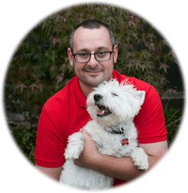 Guy wearing a red polo shirt holding his happy looking white dog.